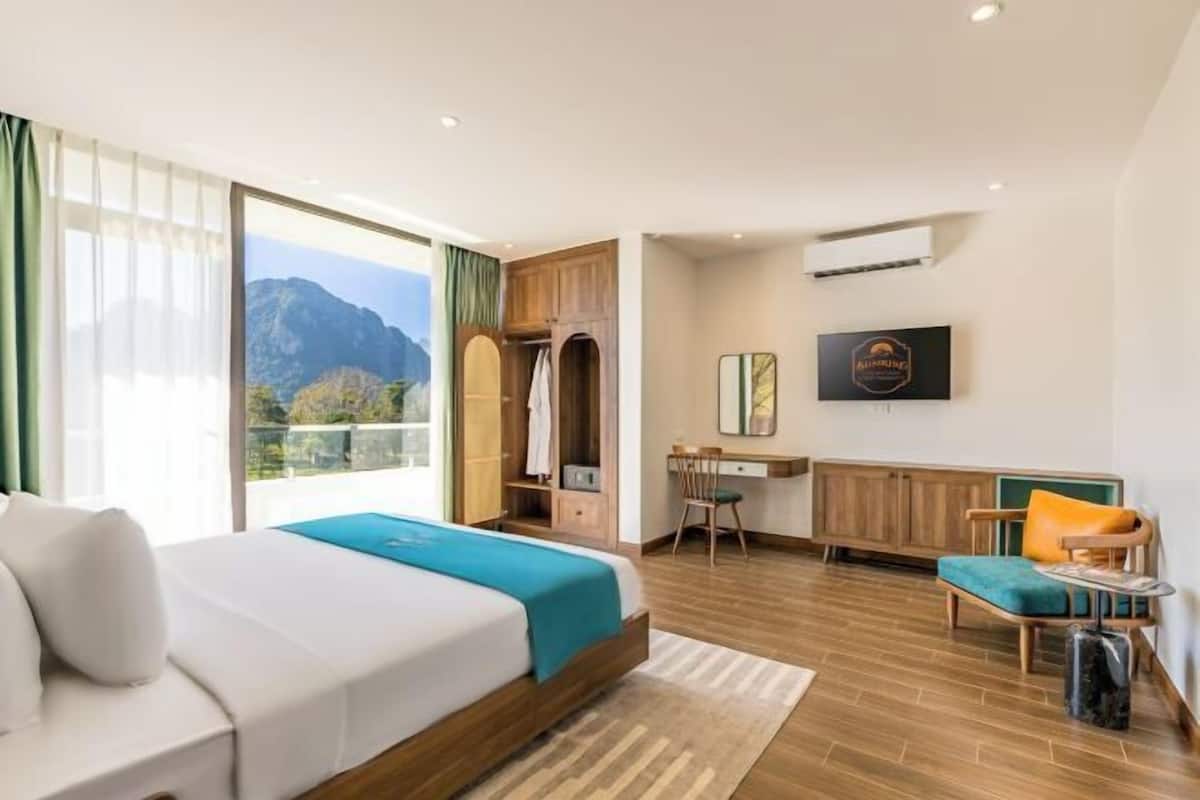 A hotel room with a bed, a desk, a chair, a TV, and a view of mountains.