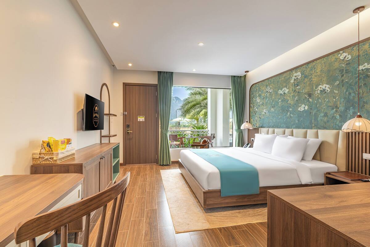 A hotel room with a bed, a desk, a chair, a TV, and a view of the outdoors.