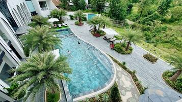A swimming pool surrounded by palm trees and benches, with a pathway leading to a building.