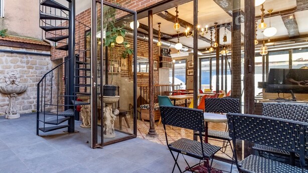 A modern outdoor dining area with a glass wall, metal staircase, and brick walls. - FRATERNITY-HOTEL (Paris)