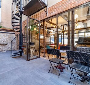 A modern outdoor dining area with a glass wall, metal staircase, and brick walls. - FRATERNITY-HOTEL (Paris)