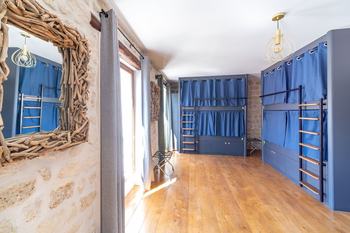 Une chambre avec des lits superposés, un plancher en bois, un mur en pierre et un miroir rustique.