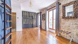 A spacious room with wooden flooring, a metal ladder, a hanging light fixture, and a stone wall. - FRATERNITY-HOTEL (Paris)