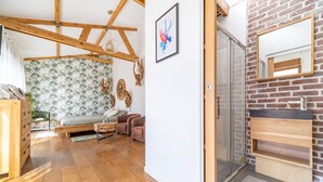 A room with wooden flooring, a bed, a sofa, a small table, and a brick wall with a mirror. - FRATERNITY-HOTEL (Paris)