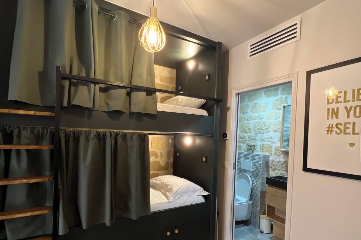 Un lit superposé avec une échelle en bois, un luminaire suspendu et une citation inspirante encadrée au mur.