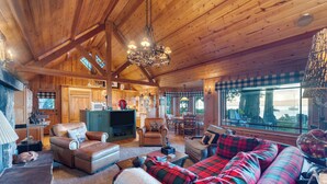 A spacious log cabin interior with a cozy living area, a fireplace, and large windows offering a view of the outdoors. - Homewood Lakefront by AvantStay | Private Beach & Lake Access + Views! (Homewood)