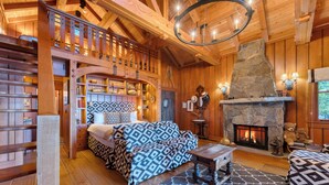 A cozy log cabin interior with a fireplace, a loft bedroom with a bed, and wooden furnishings. - Homewood Lakefront by AvantStay | Private Beach & Lake Access + Views! (Homewood)