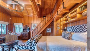A cozy log cabin interior with a large bed, a wooden staircase, and a dining area. - Homewood Lakefront by AvantStay | Private Beach & Lake Access + Views! (Homewood)