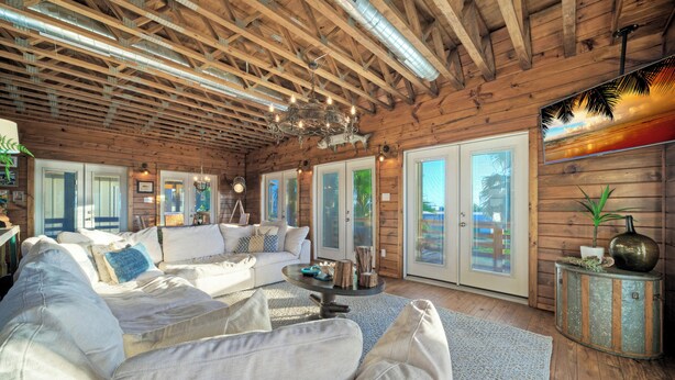 Ein geräumiges Wohnzimmer mit einem großen weißen Sofa, einem Couchtisch und einer Chandelier. Holzvertäfelte Wände und ein großes Fenster mit Aussicht.