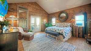 Ein Schlafzimmer mit Holzwänden, einem großen Bett mit gemusterten Betttextilien, einer Chandelieber und einem Fernseher links.