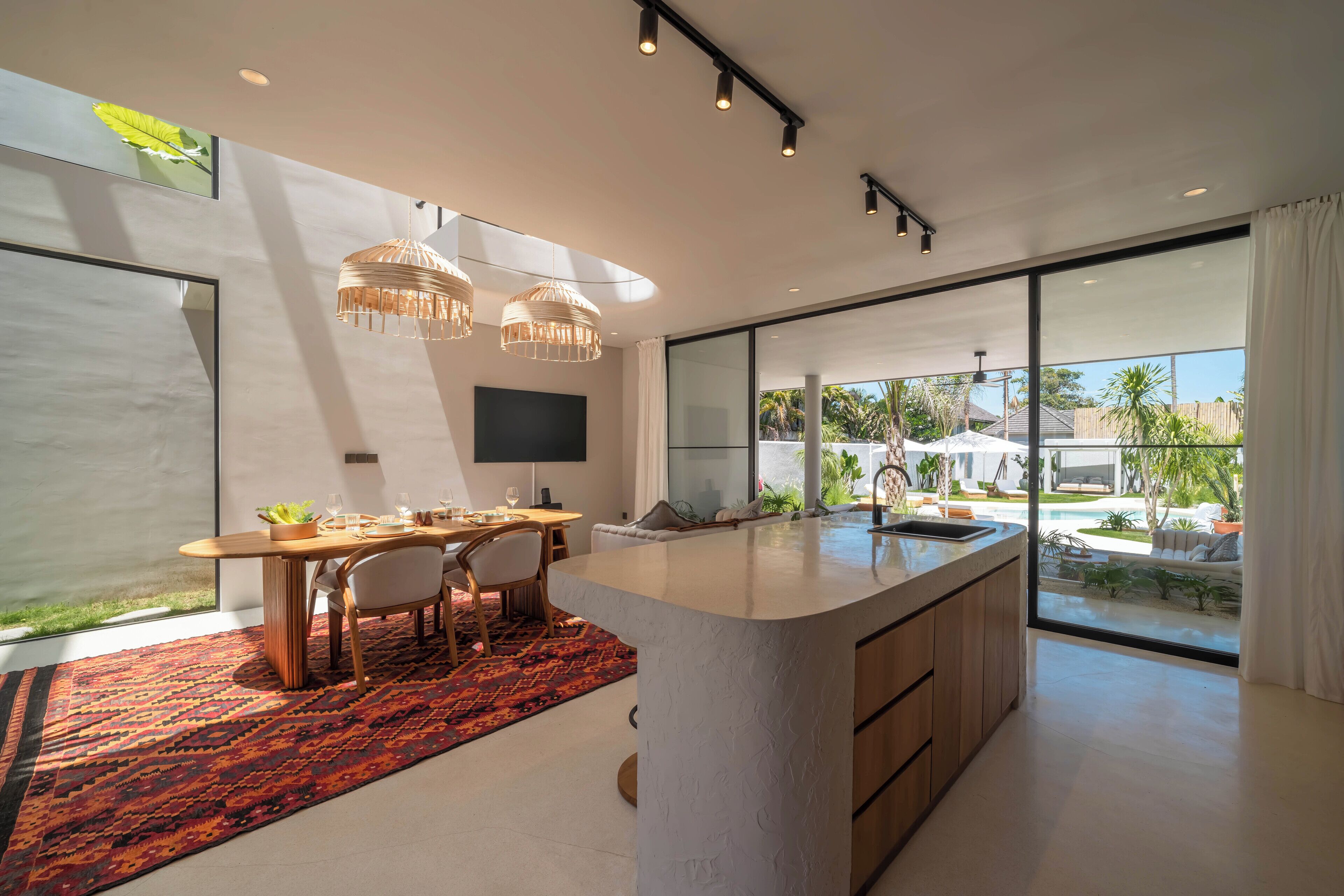 Une cuisine moderne dotée d’un grand îlot central, d’un coin repas avec une table et des chaises, et offrant une vue sur une piscine et un espace extérieur.