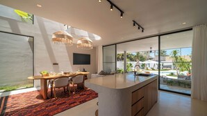 Una cocina moderna con una isla grande, un comedor con mesa y sillas, y vistas a una piscina y zona exterior.