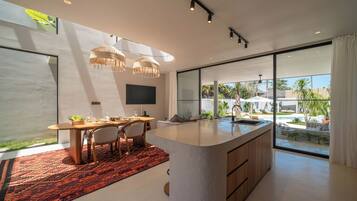 Une cuisine moderne dotée d’un grand îlot central, d’un coin repas avec une table et des chaises, et offrant une vue sur une piscine et un espace extérieur.