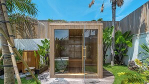 Un área de ducha exterior moderna con recinto de vidrio, rodeada de abundante vegetación y una terraza de madera.