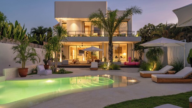 Una casa moderna de dos pisos con piscina, mobiliario exterior y exuberante jardinería.