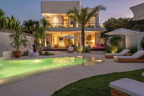 Una casa moderna de dos pisos con piscina, mobiliario exterior y exuberante jardinería.