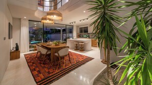 Una cocina moderna con una isla central, un área de comedor con alfombra estampada y una planta grande en maceta.
