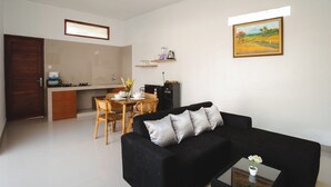 Una sala de estar moderna con un sofá negro, una mesa de comedor con sillas y una cocina con estufa y armarios.