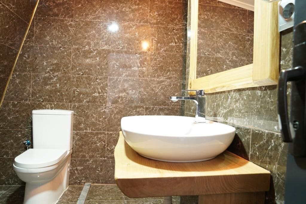 Un baño con inodoro, un lavamanos blanco sobre una encimera de madera y un espejo sobre el lavamanos.