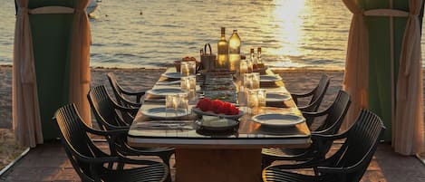 An outdoor dining area with a table set for six, overlooking a body of water at sunset.