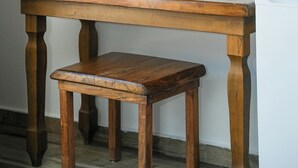 Una mesa de madera con un espejo encima, un banco delante y una puerta al fondo.