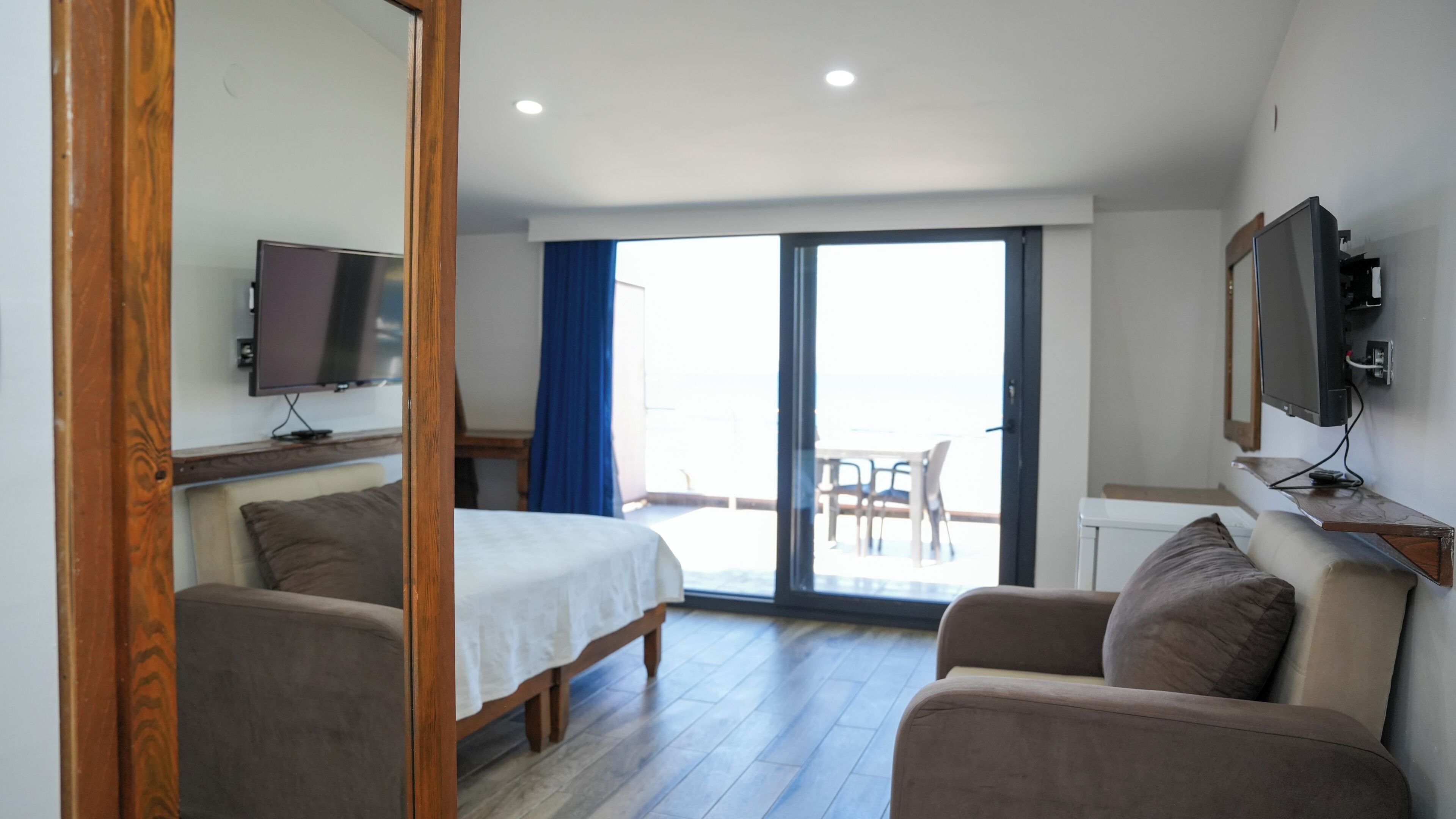 A hotel room with a bed, a sofa, a TV, and a balcony with a table and chairs.