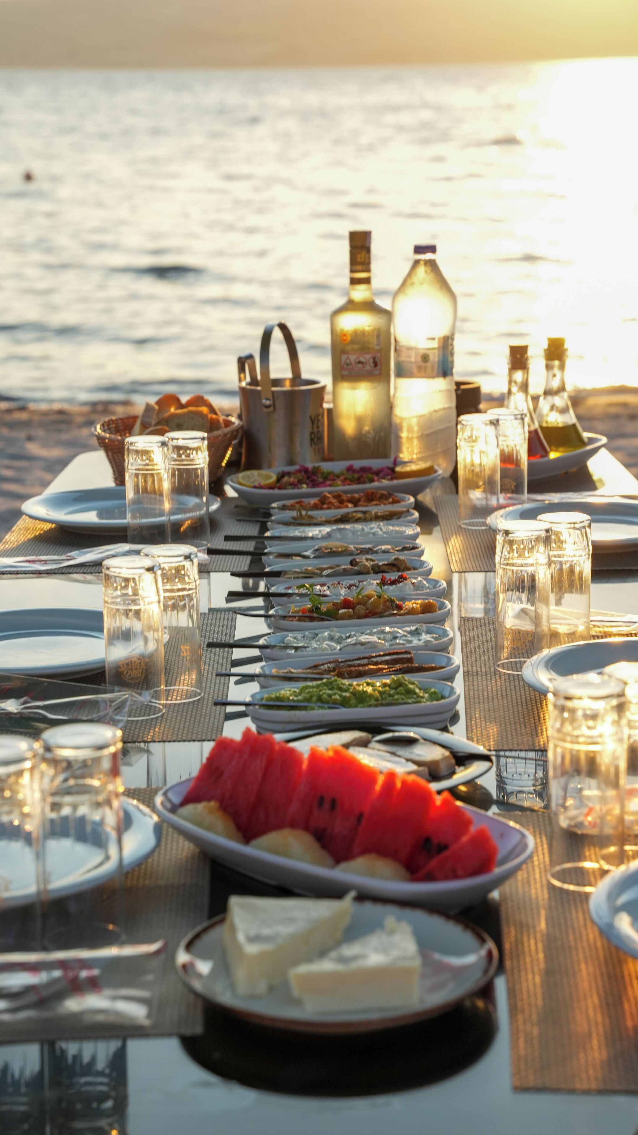 A table set for a meal with various dishes, glasses, and bottles, overlooking a body of water.
