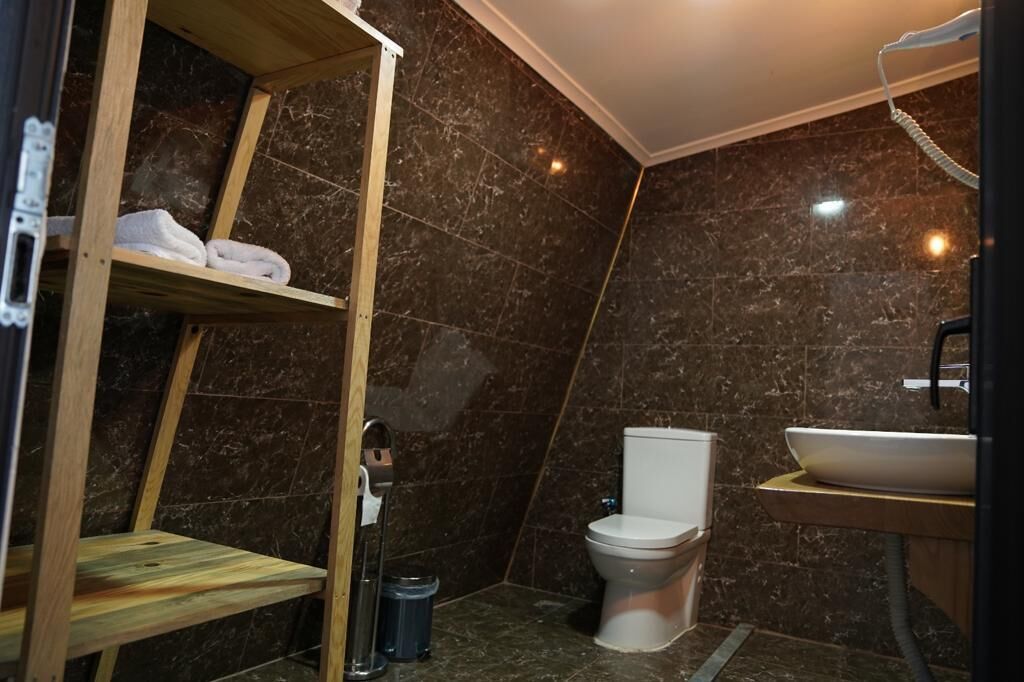 A bathroom with a marble wall, a white toilet, a wooden shelf with towels, and a sink.