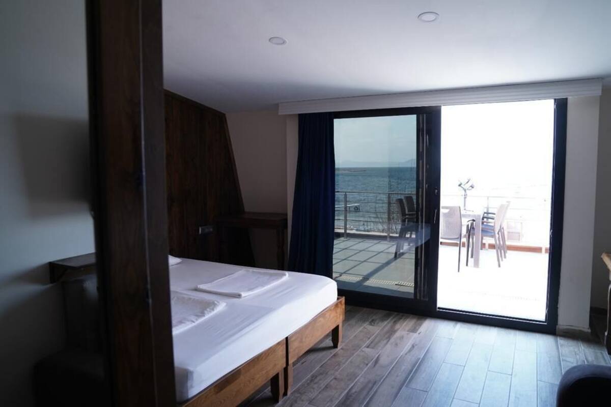 A bedroom with a bed, a desk, and a view of the sea through a sliding glass door.