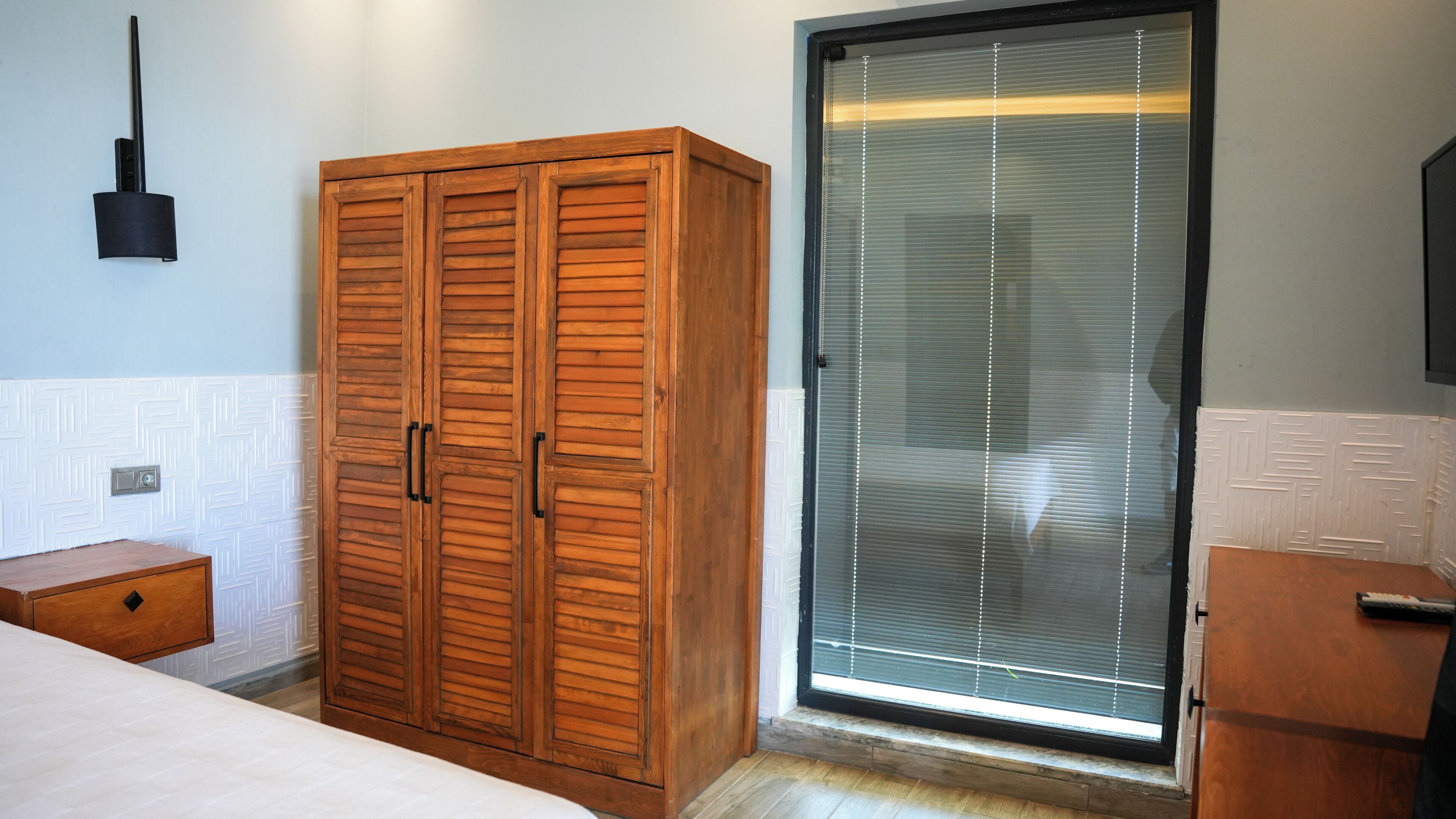 A bedroom with a wooden wardrobe, a bedside table, and a sliding glass door leading to a balcony.
