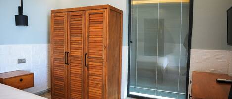 A bedroom with a wooden wardrobe, a bedside table, and a sliding glass door leading to a balcony.