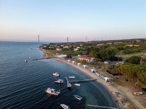 A coastal area with boats docked along the shore, a bridge in the distance, and a mix of residential and commercial buildings. - ASTROIA HOTEL (Lapseki)