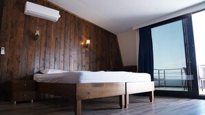 A bedroom with a wooden headboard, a bed, a nightstand, and a large window with a view of the sea. - ASTROİA OTEL & BİLİM KAMPI (Lapseki)