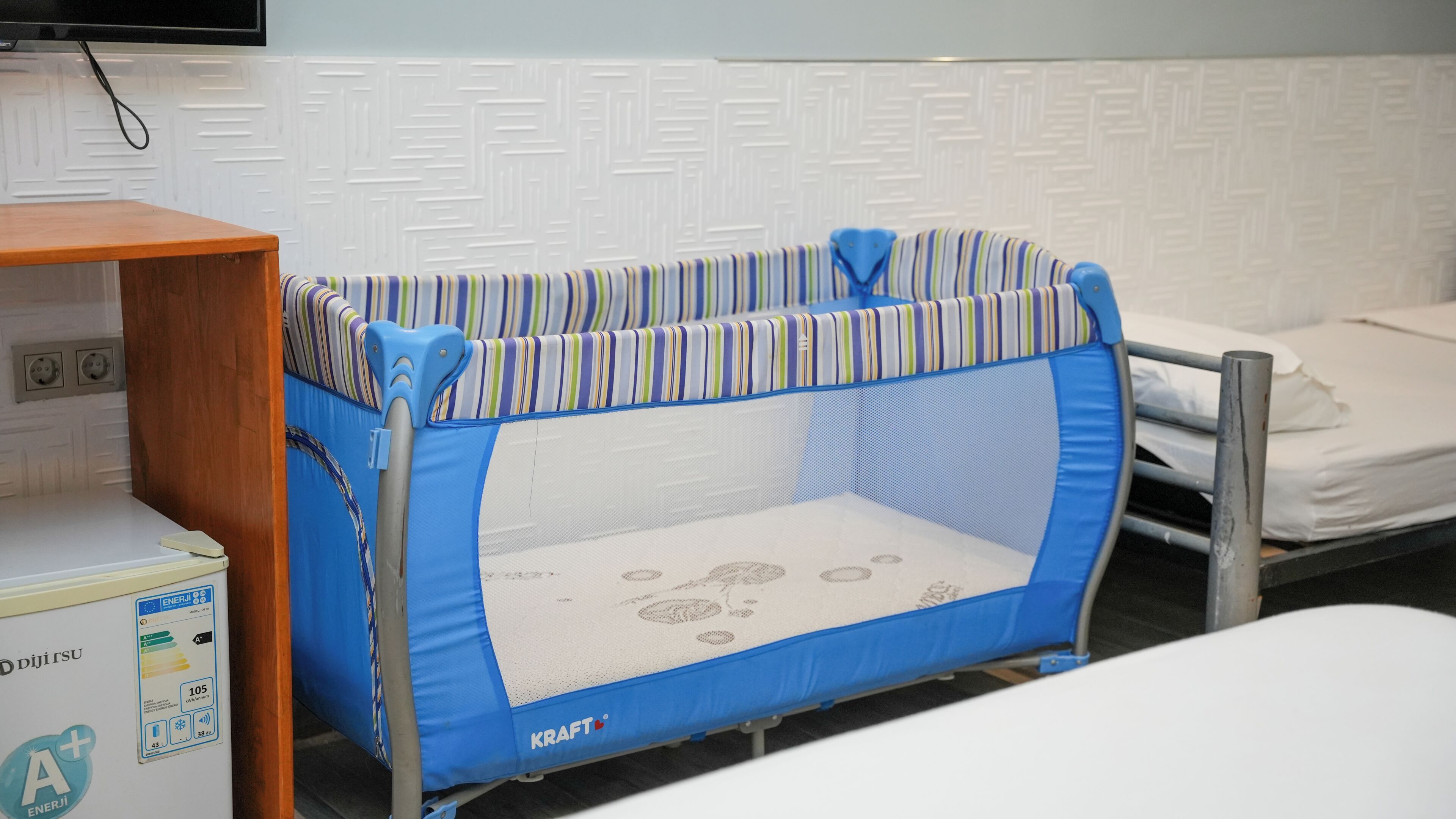 A baby playpen with a striped pattern, a power outlet, and a bed with a white mattress.
