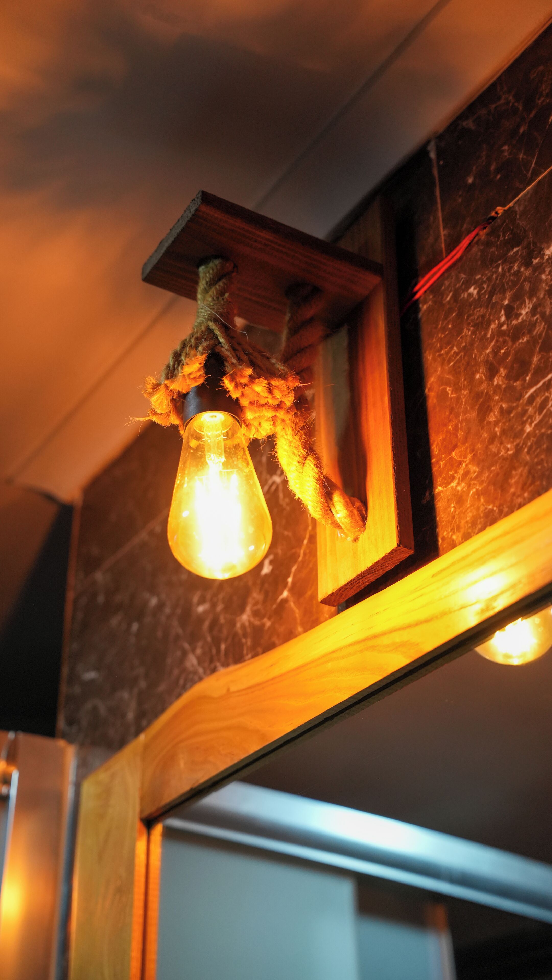 Una lámpara colgante con bombilla, marco de madera y decoración de cuerda texturizada.