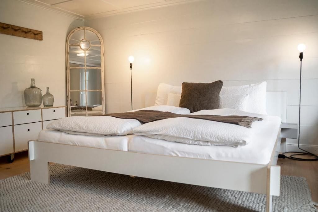 A neatly arranged bedroom with a bed, bedside tables, a mirror, and a wardrobe.