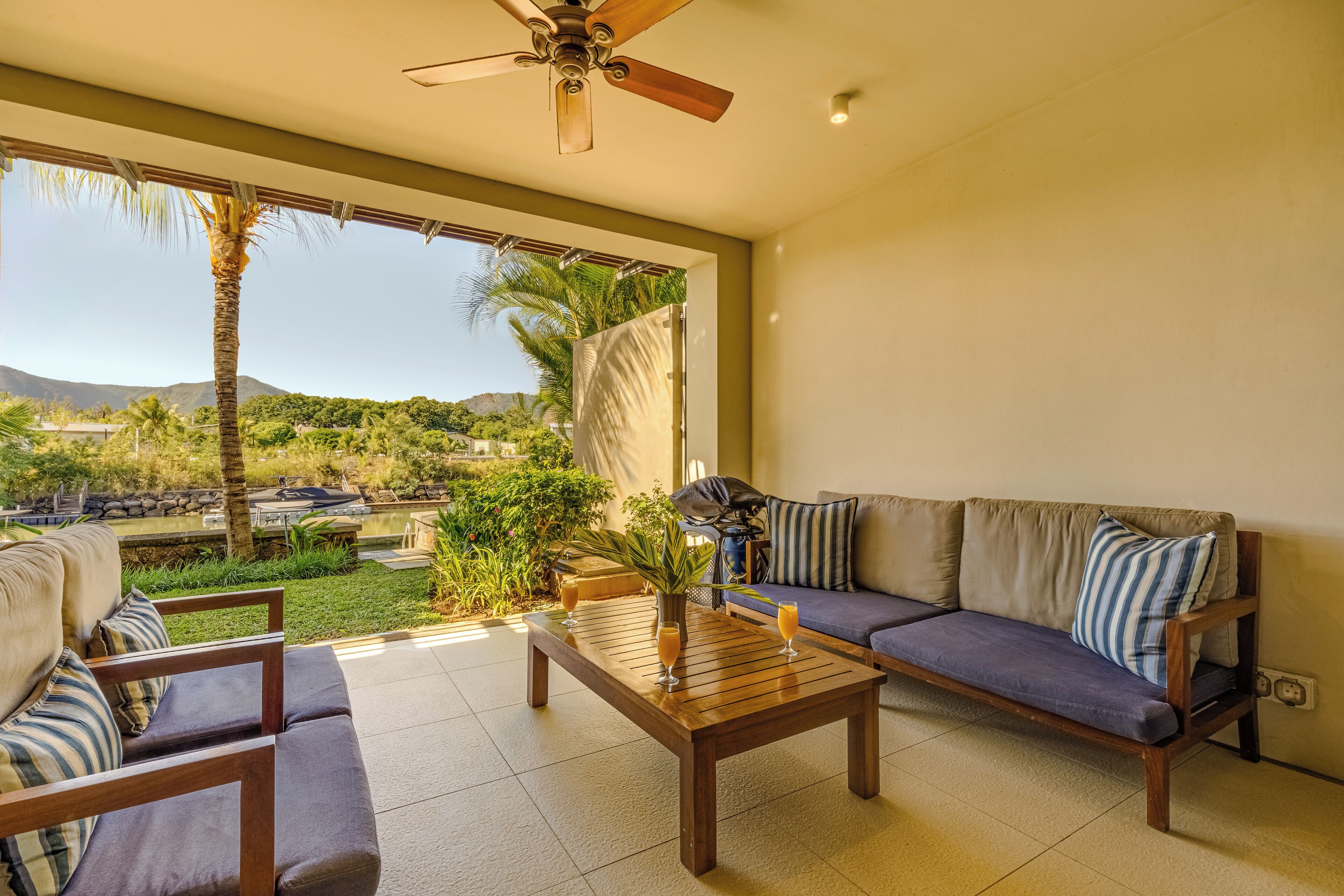 A spacious balcony with a wooden table, two sofas, and a ceiling fan.
