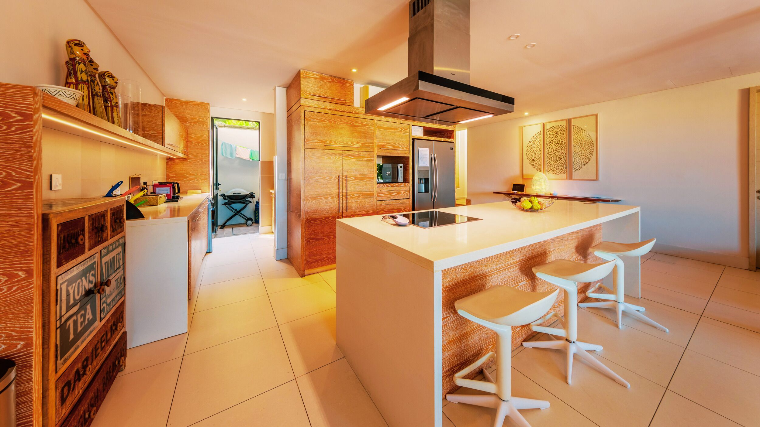 Une cuisine moderne dotée d’un îlot central, de tabourets de bar, de meubles de rangement en bois et d’un réfrigérateur visible.