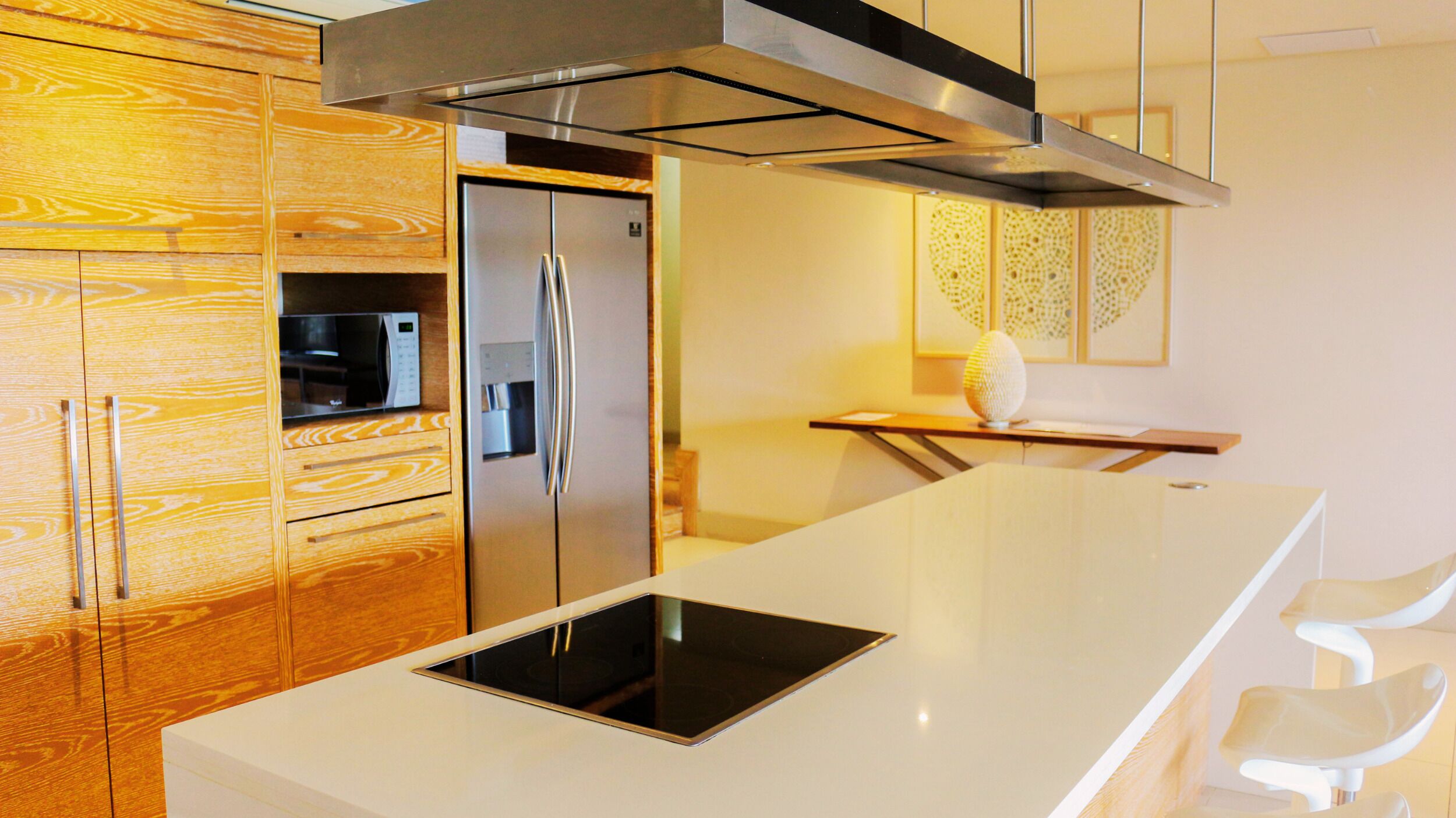 A modern kitchen with wooden cabinetry, a stainless steel refrigerator, a built-in microwave, and a sleek island with a black induction cooktop.