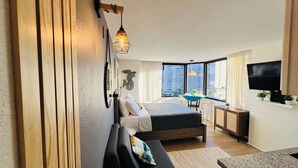 A modern hotel room with a bed, a desk, a TV, and a view of the city.