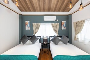 Ein Doppelzimmer mit zwei Betten, einem kleinen Tisch, einer Klimaanlage und einem Fenster mit Vorhängen.