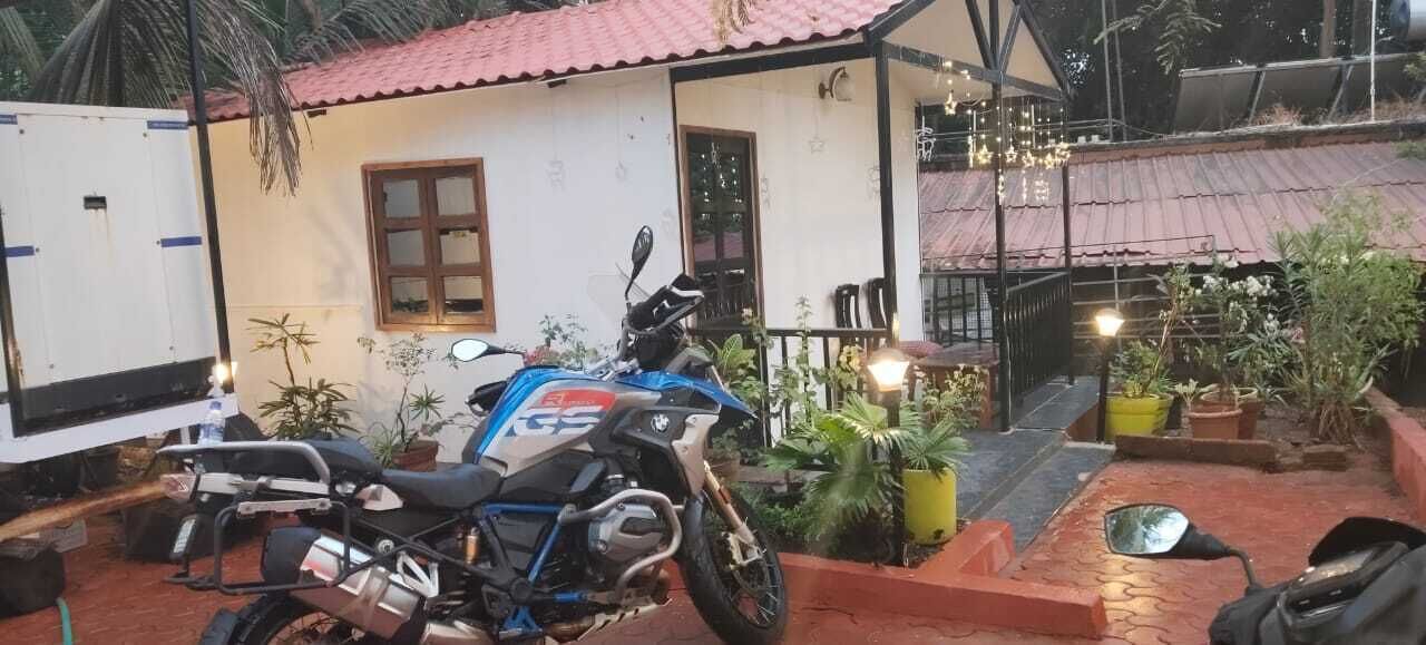 A small house with a red roof, a motorcycle parked in front, and several potted plants around.