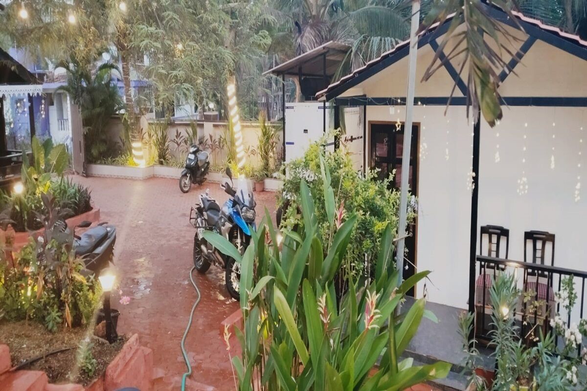A courtyard with potted plants, a motorcycle, and a small building with a table and chairs.