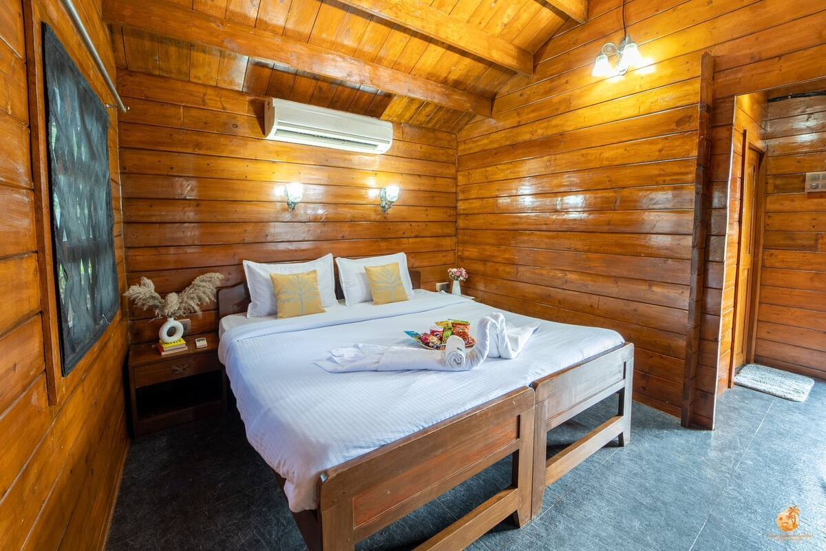 A wooden cabin bedroom with a bed, bedside tables, and an air conditioning unit.