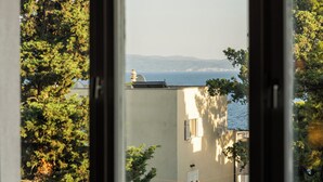 A view through a window of a building with a view of the sea and trees. - Sun Spalato Firule (Split)