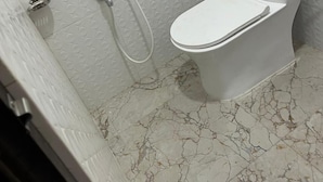 A bathroom with a white toilet, a shower, and a marble floor. - Sindura Lodge (Gop)