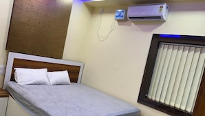 A neatly made bed with a wooden headboard, an air conditioning unit, and a window with blinds. - Sindura Lodge (Gop)