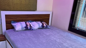 A bed with a wooden headboard, a grey mattress, and two pillows with a person on them. - Sindura Lodge (Gop)