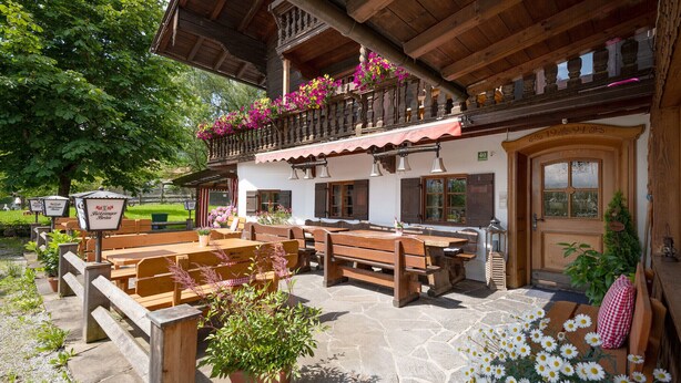 An outdoor seating area with wooden benches and tables, surrounded by potted plants and flowers. - Vacation apartment Hirschgwai 50sqm with balcony (Oberaudorf)