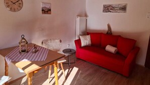 A cozy living room with a wooden table, a red sofa, a clock, and two framed pictures on the walls. - Vacation apartment Hirschgwai 50sqm with balcony (Oberaudorf)